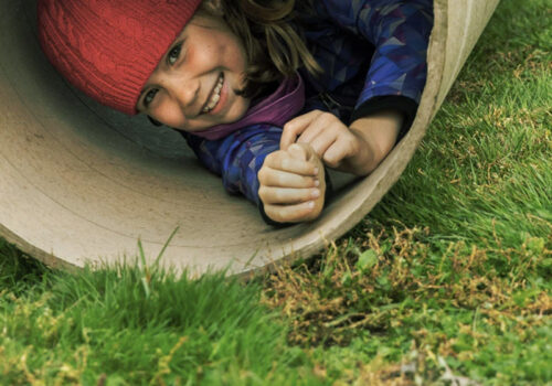 photo of a young child playing in a large tube rolling on the grass