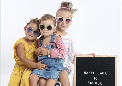 photo of three young children wearing sunglasses and oshkosh clothing with a happy back to school sign