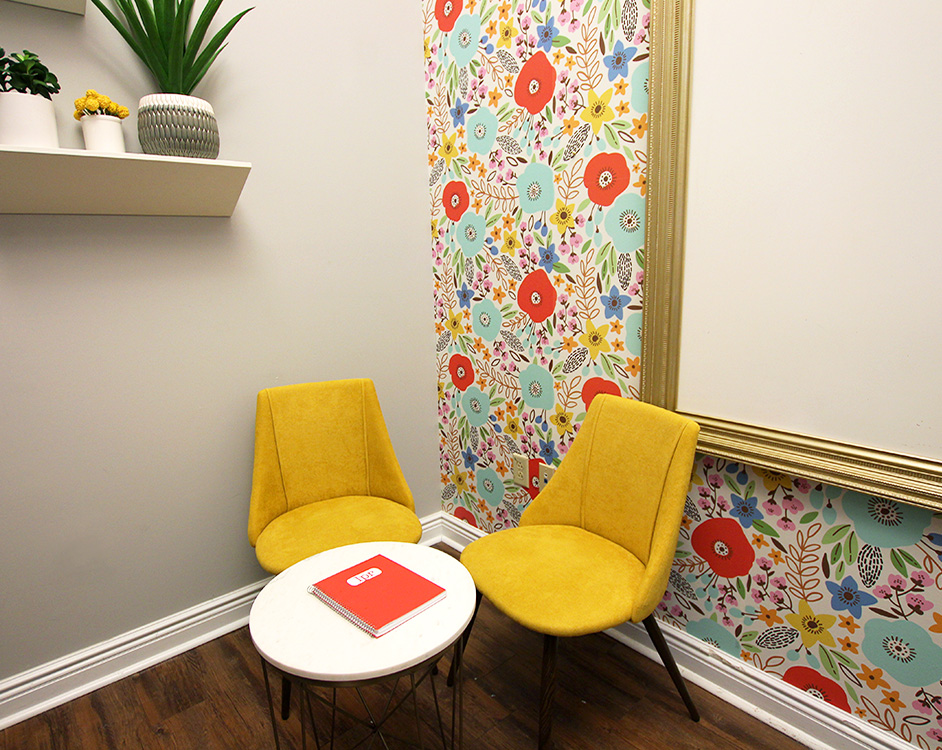 photo of two chairs and a table sitting in the corner of a room with flower wallpaper and a shelf
