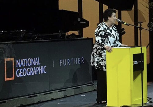 photo of a woman speaking behind a podium in front of a national geographic further sign